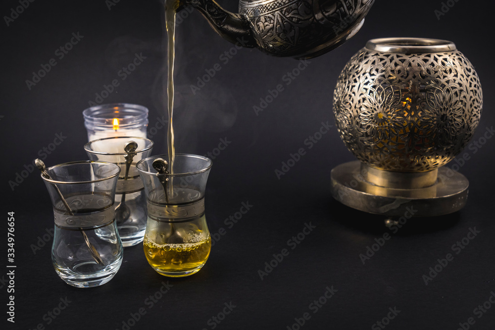 Serving green Moorish tea from a metal cup to three Turkish glasses, cup and basins on a black background Serving green Moorish tea from a metal cup to three Turkish glasses, cup and basins on a black background