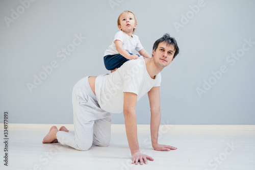 Father working out, doing single arm plank with his jolly infant baby riding on his neck. At home apartment.