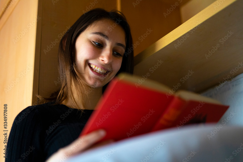 Naklejka premium Young woman reading a red book in bed.