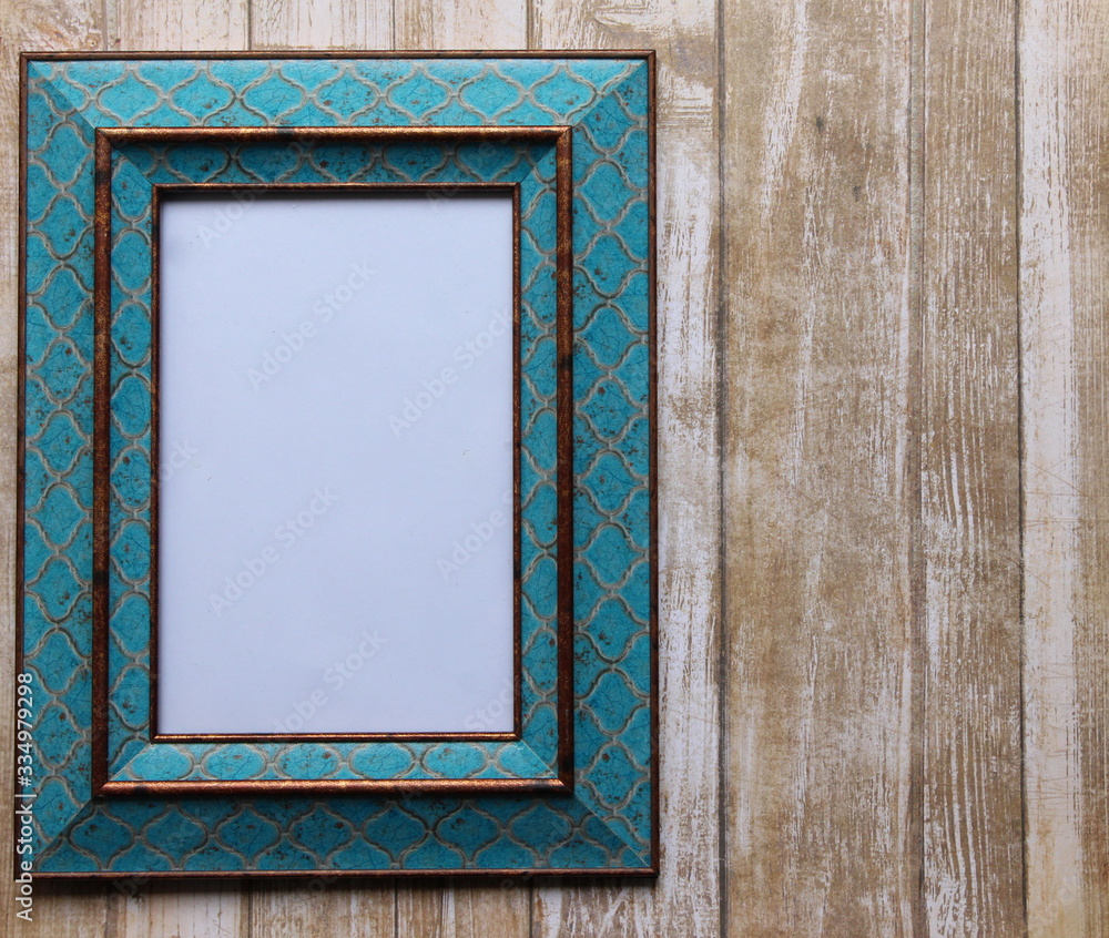 Fototapeta premium A photograph of a decorative turquoise picture frame against a wood effect background. Blank interior of the frame for your own text. Copy space. Perfect advertising or pricing frame. 