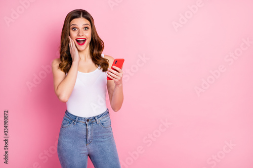 Portrait of excited energetic girl use cellphone read social media news impressed by like followers subscribers wear white singlet isolated over pink color background