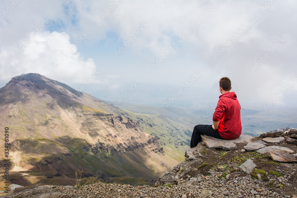 Fototapeta premium Young man sitting and looking around beautiful panoramic landscape of Mount Aragats mountain in Armenia