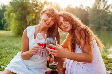 Mother's day. Mother drinking wine with her adult daughter in spring park. Family having picnic outdoors.