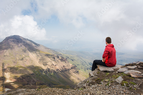 Young man sitting and looking around beautiful panoramic landscape of Mount Aragats mountain in Armenia