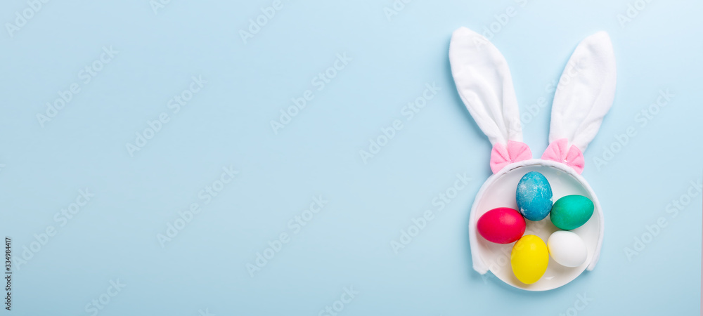 Obraz premium Cute Easter composition. Multicolored easter eggs and bunny ears on blue background. Top view. Copy space