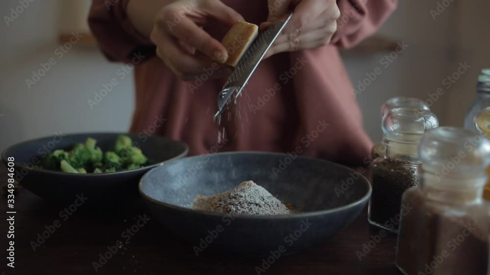 Girl rubs hard cheese on a small grater in a bowl with spices for cooking broccoli. Close-up Girl rubs hard cheese on a small grater in a bowl with spices for cooking broccoli. Close-up