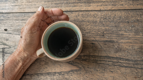 hand holding a black coffee on wooden table. ceramic round cup.
