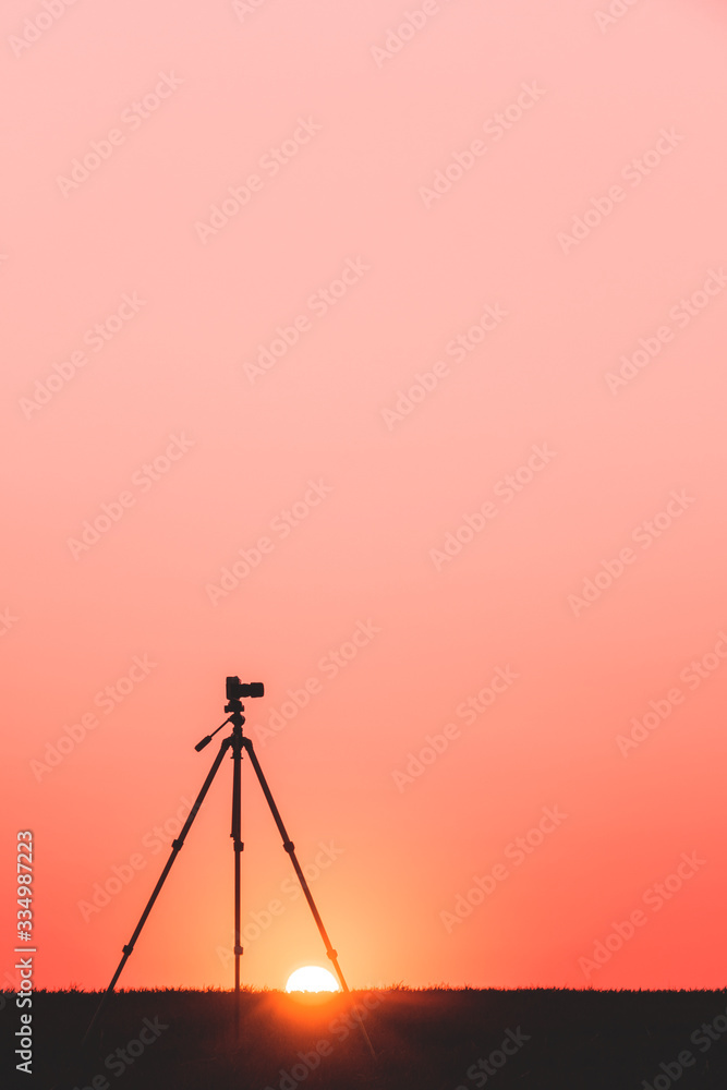 silhouette of a camera on a tripod in a field at sunset