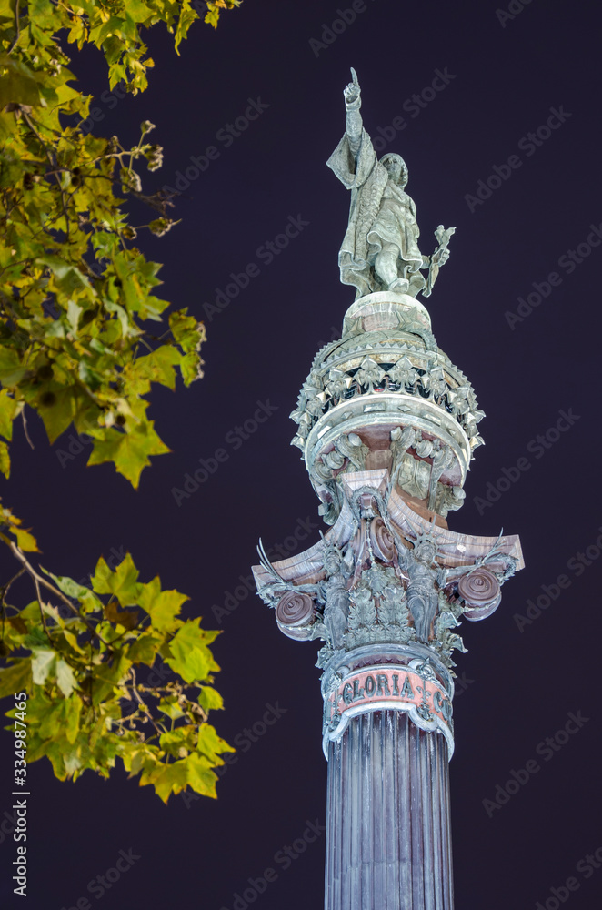 Fototapeta premium Estatua de colon de Barcelona por la noche con hojas de árbol.
