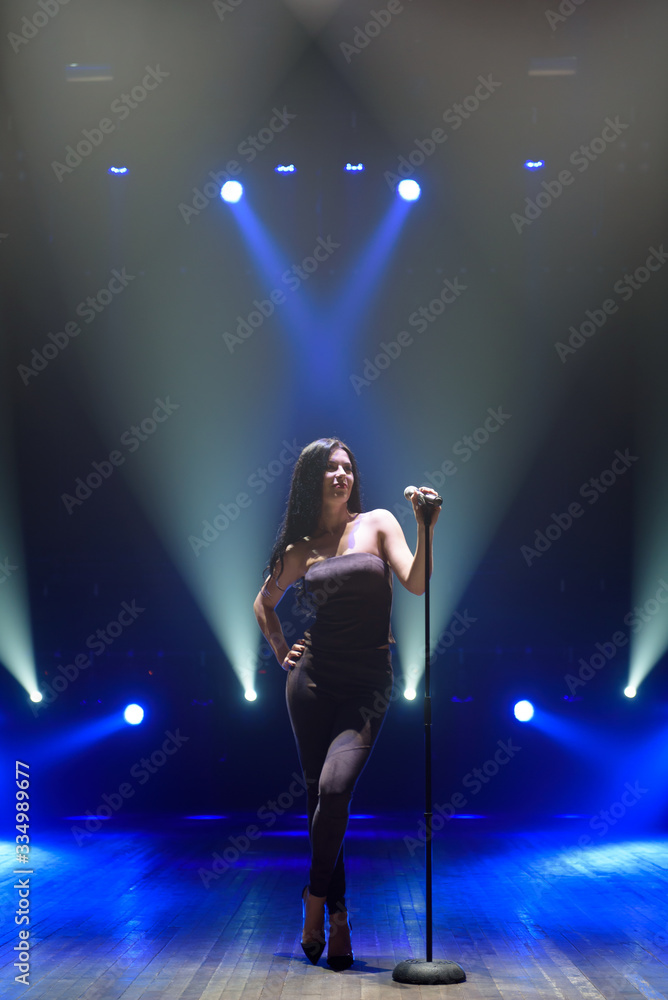 Pop musician with microphone singing a song on the stage in blue light background. Pop musician with microphone singing a song on the stage in blue light background.