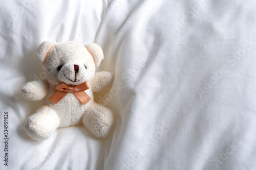 Soft beige bear, sitting on a soft white bed. Children's toy.