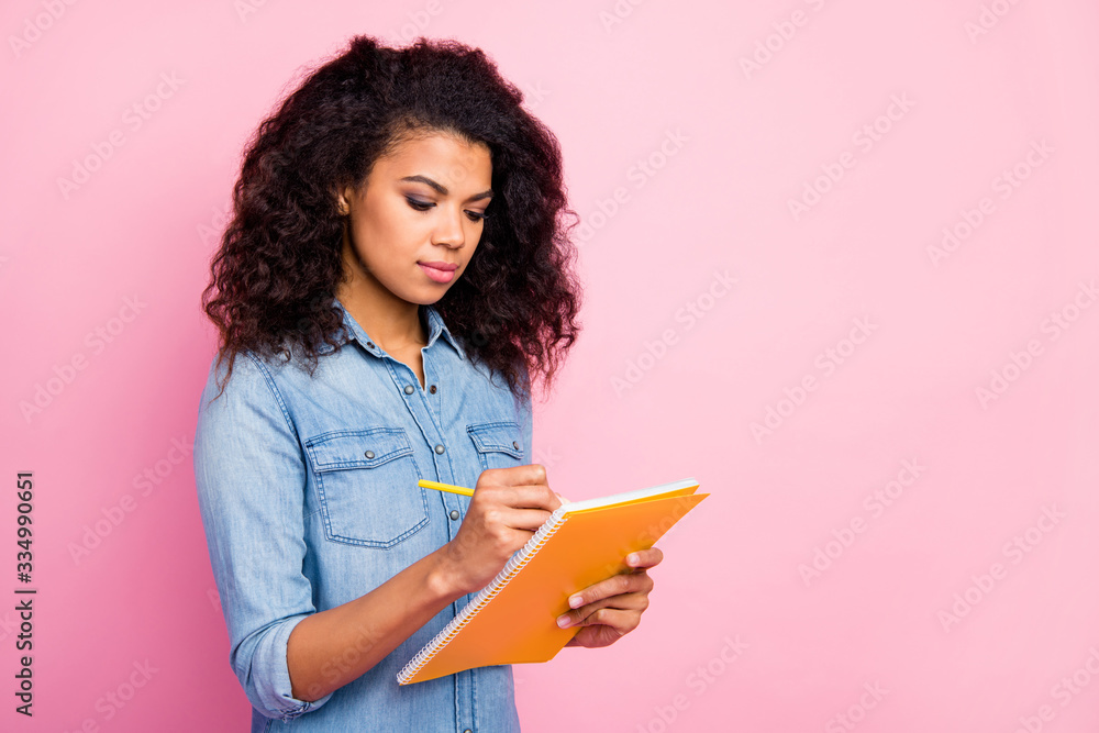Portrait of focused afro american girl write essay in copybook plan her schedule wear casual style clothing isolated over pink color background Portrait of focused afro american girl write essay in copybook plan her schedule wear casual style clothing isolated over pink color background