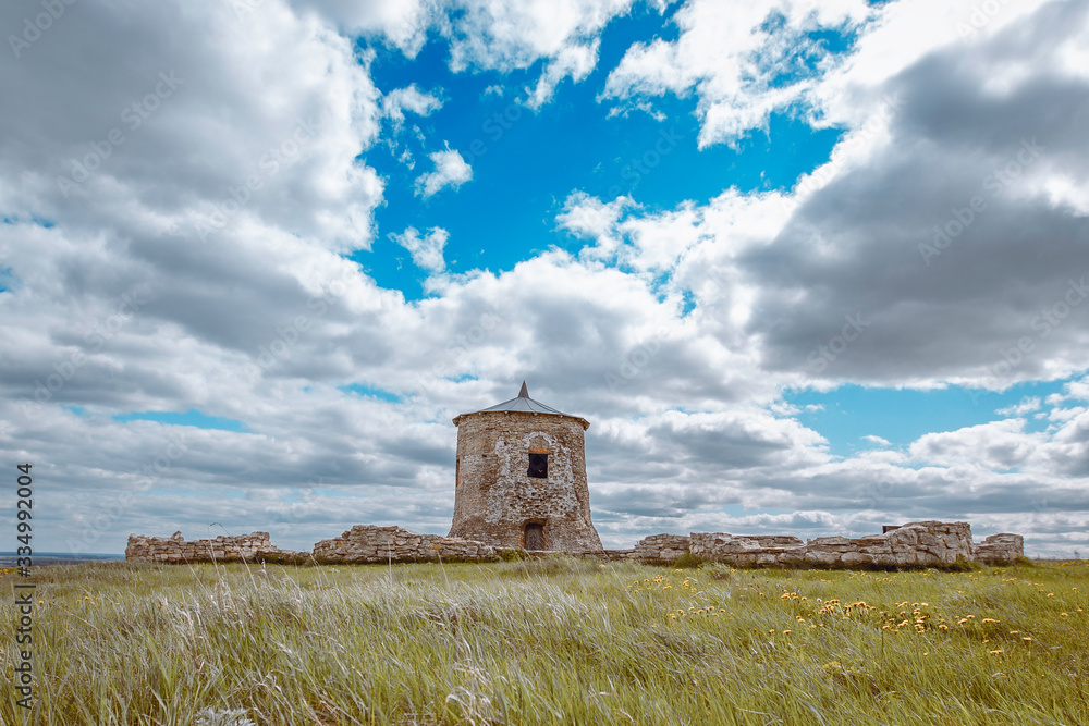 the tower and the ruined walls of the ancient fortress in Elabuga, clouds in the blue sky, steppe grass bending in the wind