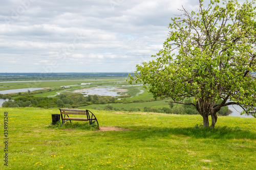 bench near a tree on the high bank of the river Kama against the background of the river and meadows