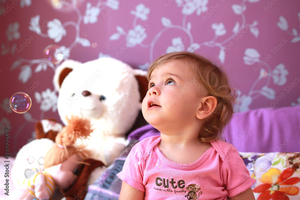 Fototapeta premium little cute caucasian girl plays in her room with soap bubbles. Children's emotions, smile and laughter. Close-up.