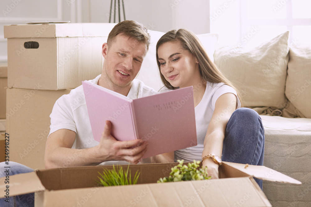 Portrait of happy couple looking at laptop computer together sitting in new house, surrounded with boxes Portrait of happy couple looking at laptop computer together sitting in new house, surrounded with boxes
