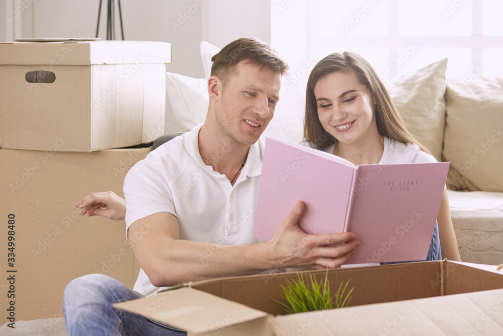 Portrait of happy couple looking at laptop computer together sitting in new house, surrounded with boxes Portrait of happy couple looking at laptop computer together sitting in new house, surrounded with boxes