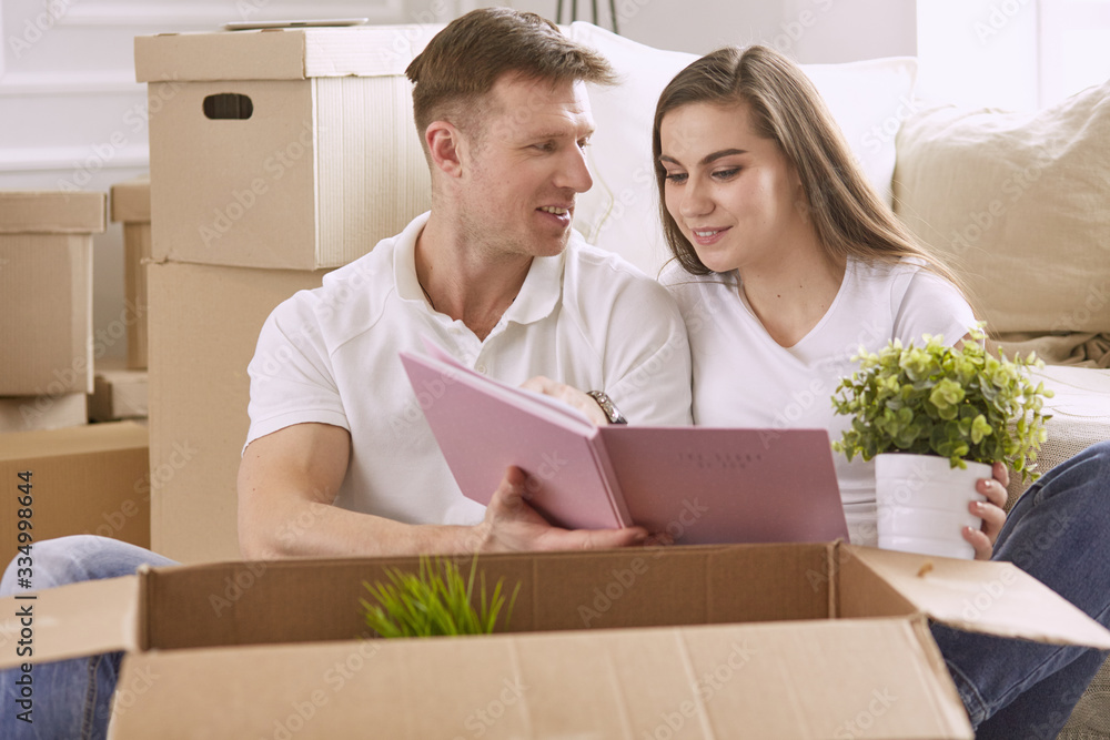 Portrait of happy couple looking at laptop computer together sitting in new house, surrounded with boxes Portrait of happy couple looking at laptop computer together sitting in new house, surrounded with boxes