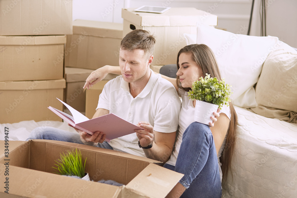 Portrait of happy couple looking at laptop computer together sitting in new house, surrounded with boxes Portrait of happy couple looking at laptop computer together sitting in new house, surrounded with boxes