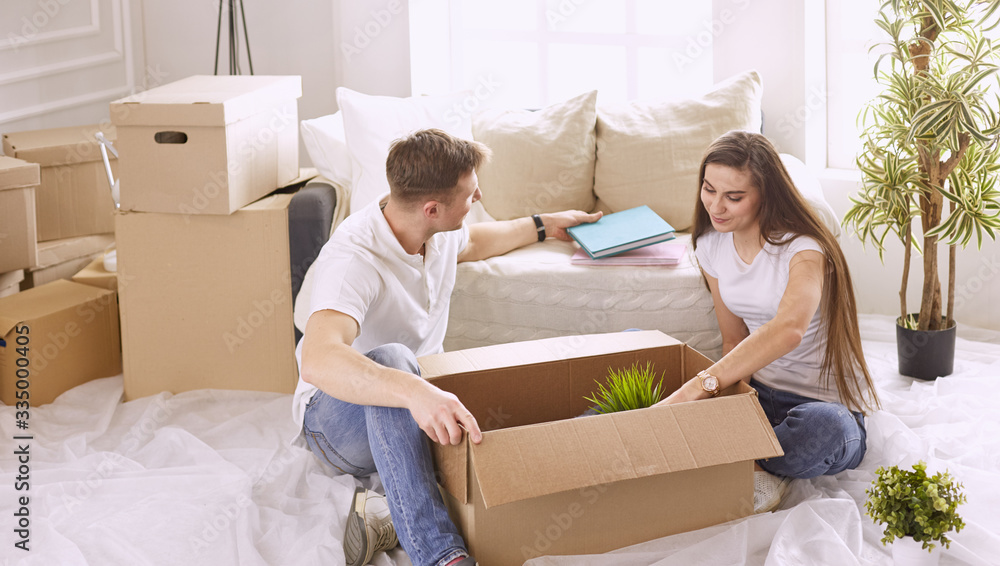 Portrait of happy couple looking at laptop computer together sitting in new house, surrounded with boxes Portrait of happy couple looking at laptop computer together sitting in new house, surrounded with boxes