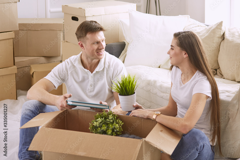 Portrait of happy couple looking at laptop computer together sitting in new house, surrounded with boxes Portrait of happy couple looking at laptop computer together sitting in new house, surrounded with boxes