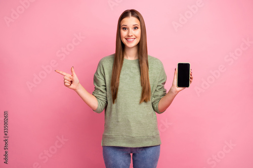 Excited style stylish girl hold cellphone search ads promotion indicate point index finger copyspace recommend suggest select wear good look jumper denim isolated pastel color background
