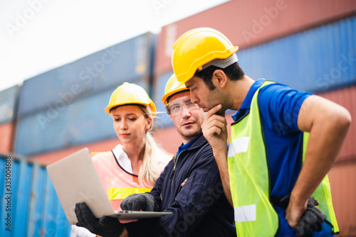 Young Caucasian man and woman group worker Check and control loading freight Containers by use computer laptop at commercial shipping dock felling happy. Cargo freight ship import export concept