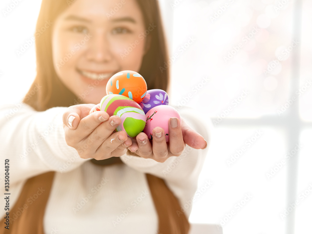 Selective focus on multicolor and design hand painted Easter Eggs on the hands with blurry background of pretty young Asian woman with copy space. Selective focus on multicolor and design hand painted Easter Eggs on the hands with blurry background of pretty young Asian woman with copy space.