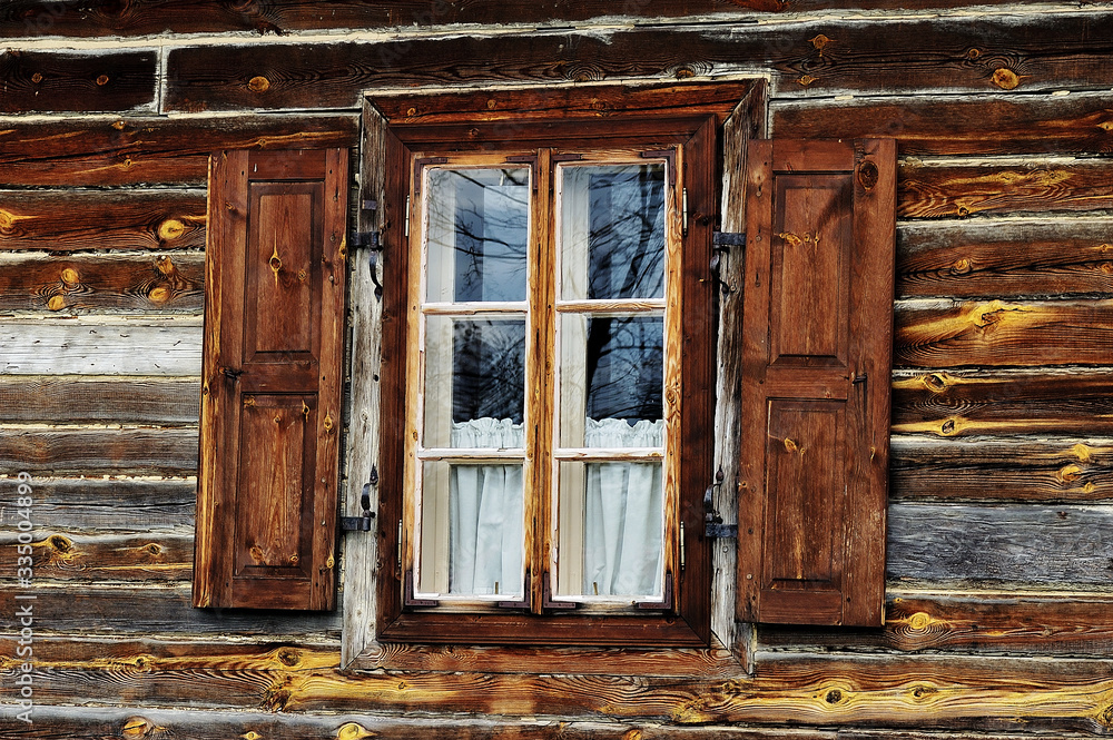 A window with open shutters on a rustic brown wooden wall. Reflection of the sky and trees in square panes. The Tokarnia open-air museum in Poland. A window with open shutters on a rustic brown wooden wall. Reflection of the sky and trees in square panes. The Tokarnia open-air museum in Poland.