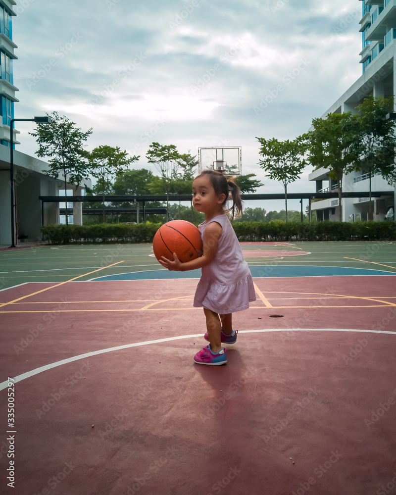 Asian Toddler playing basketball at the basketball court in the evening.
