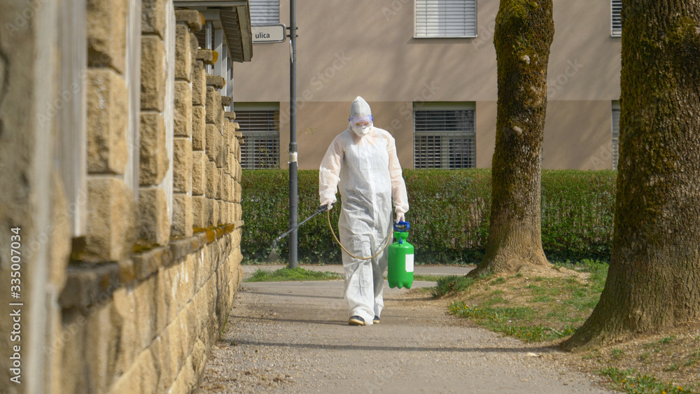SLOW MOTION: Person in a white hazmat suit sprays the sidewalk with disinfectant SLOW MOTION: Person in a white hazmat suit sprays the sidewalk with disinfectant