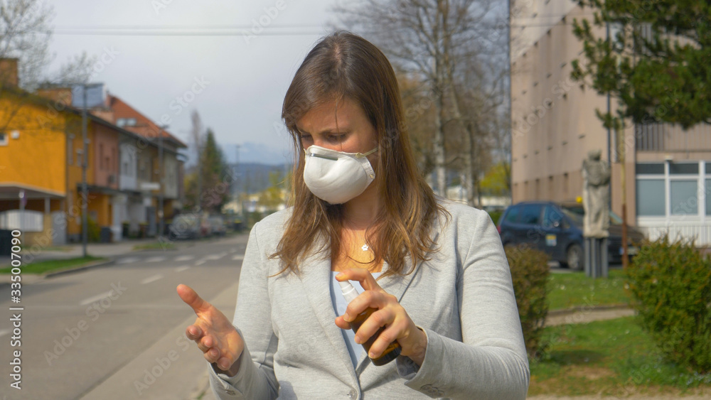 Fototapeta premium CLOSE UP: Young Caucasian businesswoman wearing a face mask sanitizes her hands.