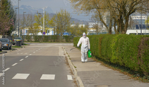 Medical specialist in a hazmat suit decontaminates a street in the suburbs.