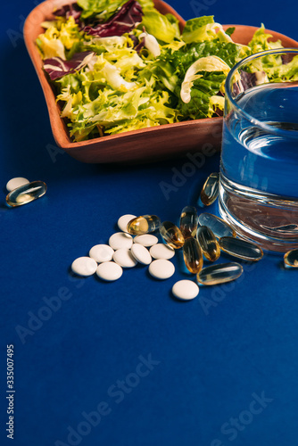 Mix of lettuce (iceberg lettuce, arugula) healthy food in a plate in the shape of a heart vegetarian, vitamins (fish oil and omega multivitamins) a glass of plain water