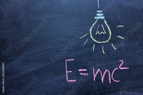 Well-known physical formula. E=mc2 on a chalk Board. Drawing of a light bulb. The concept of a sudden idea
