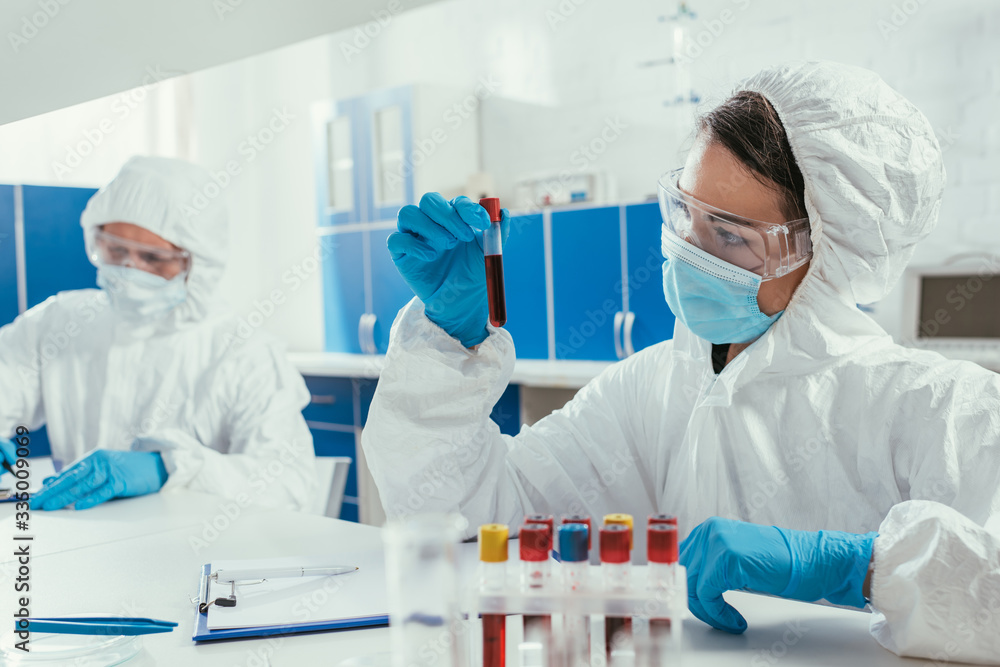 biochemist holding test tube with blood sample near colleague in laboratory biochemist holding test tube with blood sample near colleague in laboratory