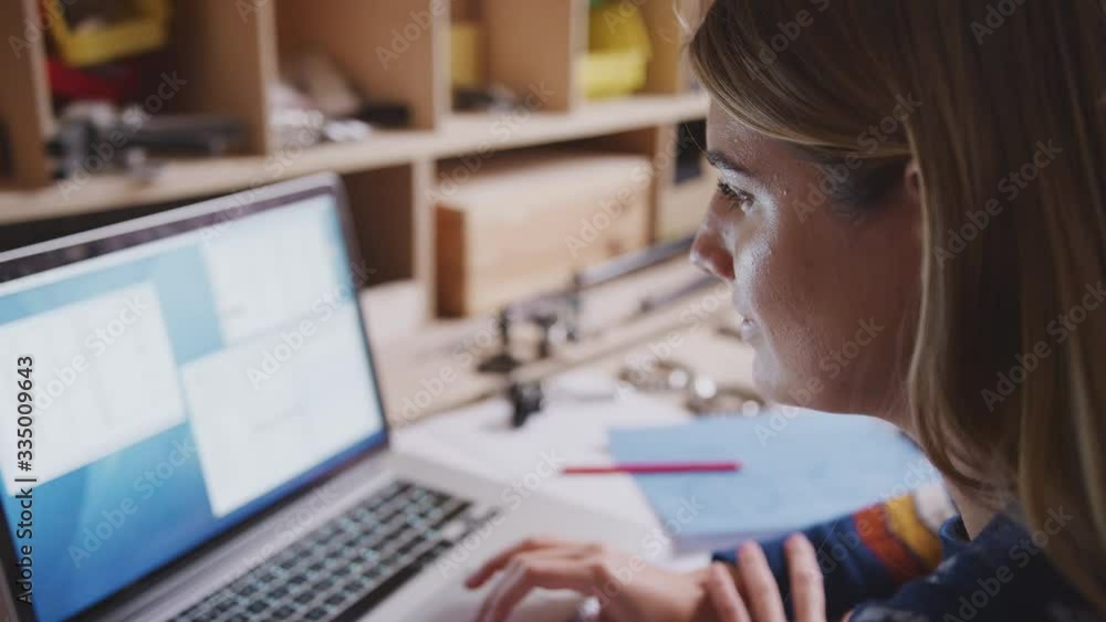 Close up of female engineer in workshop using laptop and making notes on plan for bicycle - shot in slow motion Close up of female engineer in workshop using laptop and making notes on plan for bicycle - shot in slow motion