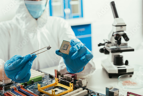 cropped view of engineer holding microchip and small stone near microscope and computer motherboard