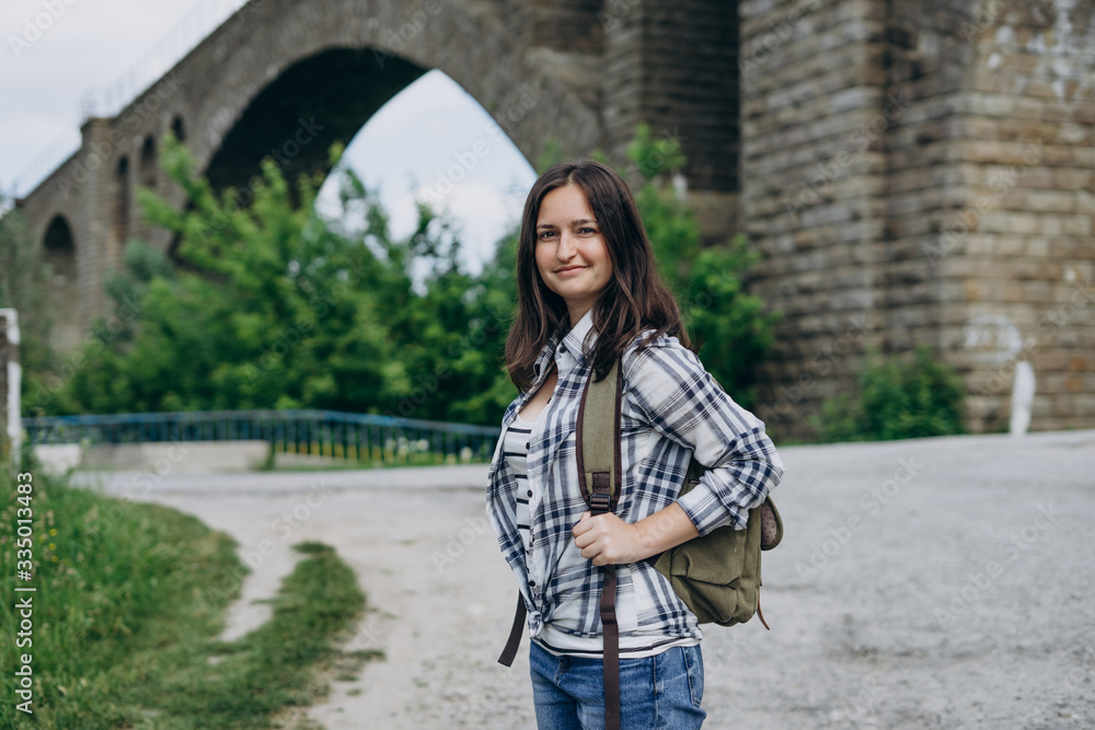 Tourist girl with a backpack on the background of the stone bridge. Girl in jeans and shirt