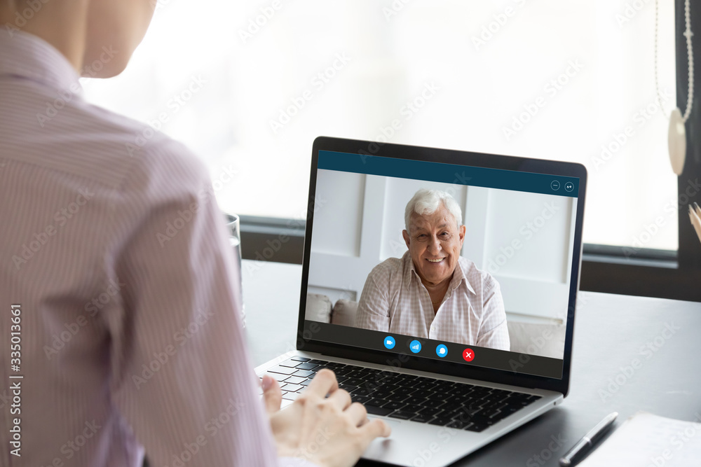 Back view of young female sit at desk in office talk on video call with smiling elderly father, loving millennial girl daughter have pleasant conversation on webcam on laptop with happy senior dad Back view of young female sit at desk in office talk on video call with smiling elderly father, loving millennial girl daughter have pleasant conversation on webcam on laptop with happy senior dad