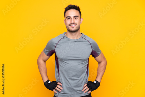 Bild auf Leinwand Sport man over isolated yellow wall posing with arms at hip and smiling