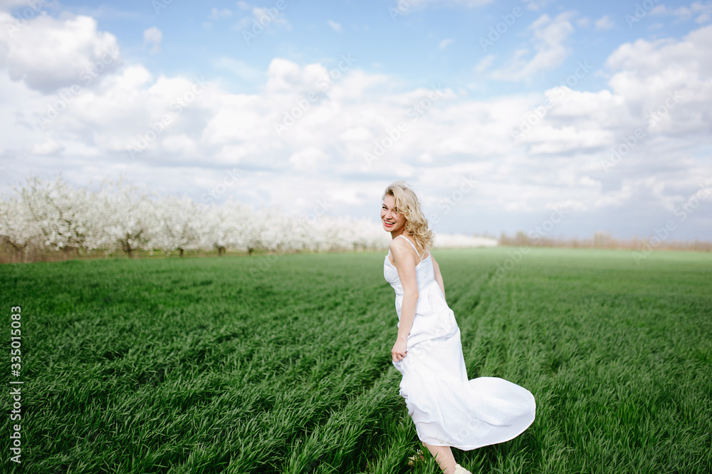 blonde girl in a white dress sits on the green fresh spring grass, blue sky blonde girl in a white dress sits on the green fresh spring grass, blue sky