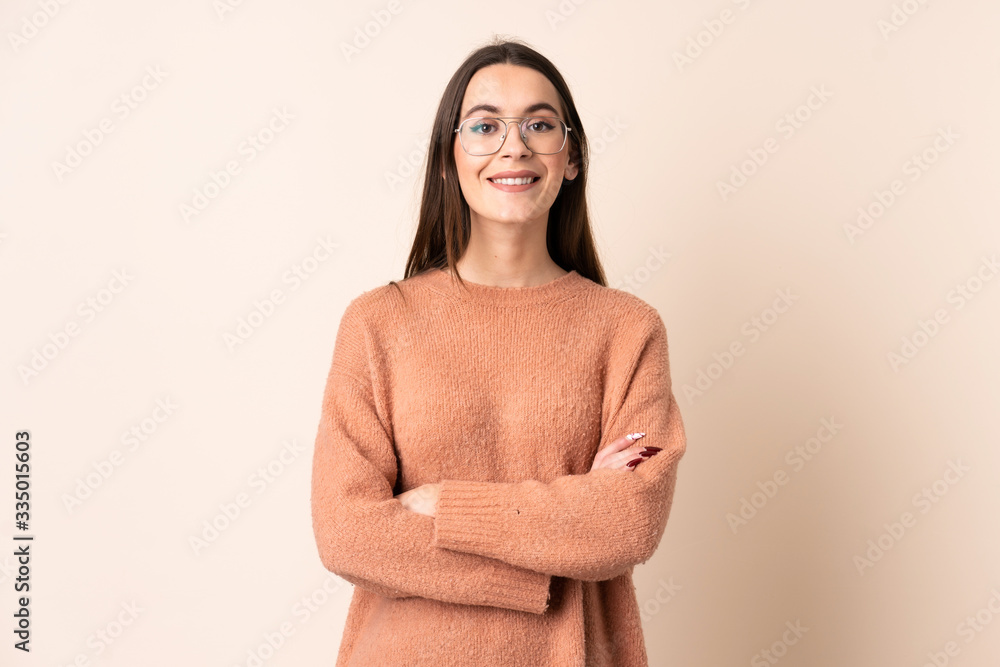 Young woman over isolated beige background keeping the arms crossed in frontal position Young woman over isolated beige background keeping the arms crossed in frontal position
