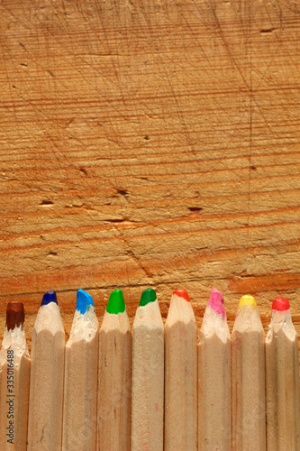 Wide multicolored wooden pencils on wooden background. Top view. (ID: 335016488)