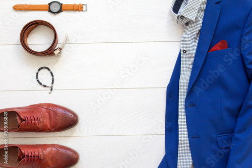 Flat lay set of classic mens clothes such as blue suit, brown shoes, belt, watches and bracelet on white wooden background. (ID: 335016849)