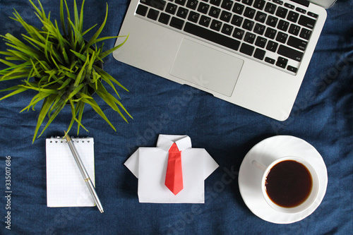 Laptop keyboard, white notepad, pen, cup of tea on saucer, white origami shirt with red tie on blue crumpled jeans background. Top view. Flat lay. (ID: 335017686)