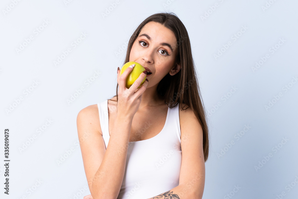 Young woman over isolated blue background eating an apple Young woman over isolated blue background eating an apple