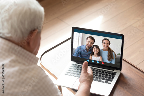 Back view of elderly grandfather talk chat on video call on computer with family and granddaughter, mature granddad have online conversation using webcam on laptop with happy relatives