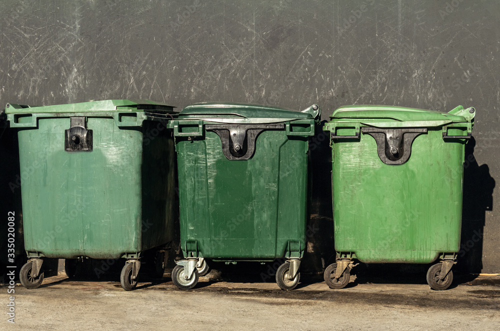 Green garbage containers stand in the city against a concrete wall. Disposal during a pandemic Green garbage containers stand in the city against a concrete wall. Disposal during a pandemic