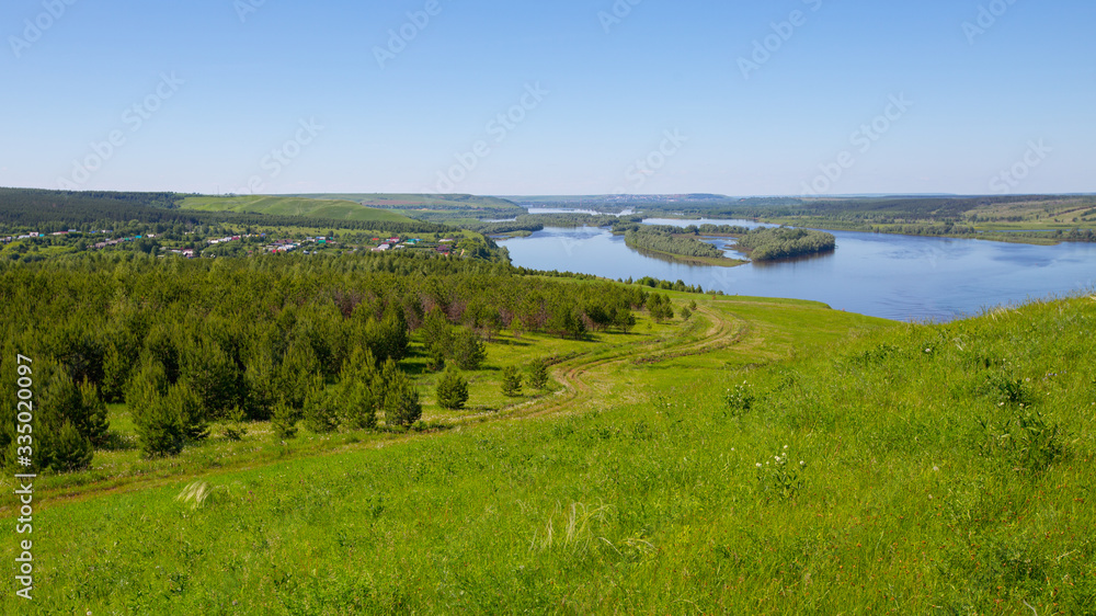 country road on a hillside overgrown with grass and sparse small trees on the banks of the Kama River